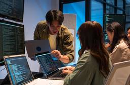 Software development team reviewing code on laptops and multiple monitors in a modern office.